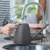 A person is filling a watering can with water from a faucet in a kitchen sink. Náhled obrázku produktu