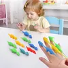 Mehrfarbige Dinosaurier-Fingerpuppen auf einem weißen Tisch, mit einer Erwachsenenhand, die einige trägt, und einem Kind, das andere ansieht Produktbild-Vorschau