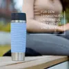A person is sitting outdoors with a blue insulated mug in the foreground. Náhled obrázku produktu
