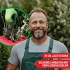 A man wearing overalls is smiling and holding a garden tool near some branches, with text overlays highlighting product features. Produktbild-Vorschau
