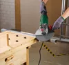 A person wearing gloves is using an angle grinder to cut a metal bar on a workbench. Produktbild-Vorschau