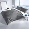 A bed with gray and white striped bedding in a modern room with large windows. Produktbild-Vorschau