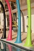 Four colorful outdoor showers are lined up next to a swimming pool. Produktbild-Vorschau