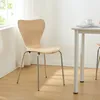 A wooden chair with chrome legs is placed next to a white table in a room with a window and white curtains. Voir les images du produit