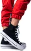 A close-up shot of a person's feet wearing black Converse Chuck Taylor All Star platform high-top sneakers and red track pants. Voir les images du produit