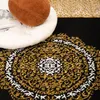 A close-up view of a rug with an intricate oriental pattern in black, gold, and white. A white cushion and a brown pillow are partially visible in the upper left corner. Voir les images du produit