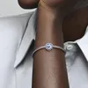 A close-up shot of a person's arm wearing a Pandora charm bracelet with a blue and purple flower charm. Anteprima dell’immagine prodotto