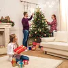 A family is decorating a Christmas tree in a living room, with gifts around the tree and a fireplace in the background. Produktbild-Vorschau