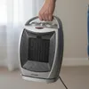 A person is holding a portable electric heater. Podgląd zdjęcia produktu