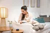 A woman is relaxing on a couch and interacting with a smart speaker. Produktbild-Vorschau