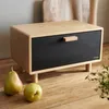 A bread box on a wooden surface with fruit in the foreground. Náhled obrázku produktu