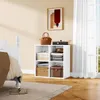 A white cube storage shelf with folded clothes, hats, and boxes inside, placed next to a white bed and in front of a window with white curtains. Náhľad obrázku produktu