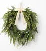 A green wreath with black berries and small white lights, adorned with a beige bow, hanging against a white background. Voir les images du produit