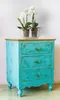 A turquoise painted wooden cabinet with three drawers and gold hardware, topped with a clear glass bowl containing two white orchid plants. Podgląd zdjęcia produktu