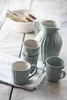 A collection of ceramic mugs and a pitcher arranged on a wooden surface with a newspaper. Produktbild-Vorschau