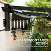 A close-up view of a black pergola bracket mounted to a wall, with mounting screws displayed in front of it. The background shows greenery and a wall. Náhľad obrázku produktu