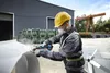 A construction worker is using an angle grinder on a large white object outdoors. Náhľad obrázku produktu