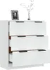 A white chest of drawers with three drawers and black handles. A framed photo and a vase with a plant are on top. Produktbild-Vorschau