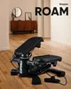 A black stepper machine is placed on a wooden floor in a room with furniture in the background. Podgląd zdjęcia produktu