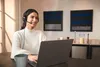 A woman wearing a headset is working on a laptop in a well-lit room. Podgląd zdjęcia produktu