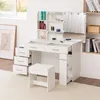 A white vanity table with a mirror and lights, and a matching stool, set up in a room with a window and bookshelves. Produktbild-Vorschau