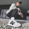 A man is crouching on a rocky surface, wearing New Balance sneakers. Voir les images du produit