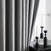 A close-up view of gray curtains with two black candle holders and two white candles on a table next to a window. Produktbild-Vorschau