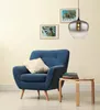 A blue armchair with a cream pillow sits next to a small wooden table with books, in front of a cream-colored wall with two framed pictures of palm trees. A pendant light hangs from the ceiling. Anteprima dell’immagine prodotto