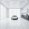 A futuristic silver car is parked in a modern, minimalist garage with large windows and hexagonal ceiling lights. Podgląd zdjęcia produktu