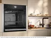 A modern kitchen scene featuring a built-in oven and a sink area with decorative items. Produktbild-Vorschau