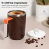 A self-stirring mug with a wood-grain finish and an orange accent on the handle, placed on a pink surface next to coffee beans and a lid. Podgląd zdjęcia produktu