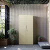 A beige metal cabinet is shown in an outdoor or patio setting, surrounded by plants and a textured wall. Náhľad obrázku produktu