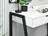 A close-up view of a white desk with black metal legs, showing a drawer, a lamp, and a plant. Voir les images du produit