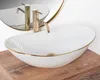 A close-up shot of a white oval basin with a gold rim and a gold faucet, placed on a wooden surface. Anteprima dell’immagine prodotto