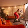 A woman is exercising on an Adidas exercise bike in a modern living room with a sofa and plants. Produktbild-Vorschau