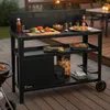 An outdoor patio setting with a black grill cart filled with grilling accessories and food. Podgląd zdjęcia produktu