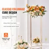 A tall, gold, geometric stand holding a large floral arrangement, with smaller floral arrangements and candles on a table. Podgląd zdjęcia produktu