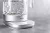 A close-up shot of a white electric kettle with water boiling inside, sitting on its charging base. Náhled obrázku produktu