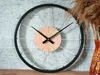 A bicycle wheel clock is displayed on a textured wall, with dried reeds in a vase to the right. Produktbild-Vorschau