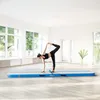 A woman is performing a yoga pose on a blue and white air track in a bright, airy room with large windows. Náhled obrázku produktu