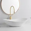 A white oval vessel sink with a gold faucet in front of a round mirror. Náhľad obrázku produktu