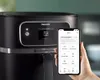 A hand holds a smartphone displaying an air fryer app next to a Philips air fryer. Podgląd zdjęcia produktu