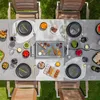 An overhead view of a raclette grill set up on a table outdoors, with food and place settings. Produktbild-Vorschau
