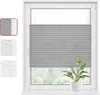 A grey pleated blind is shown installed on a white window frame. A small green plant in a white pot sits on the windowsill below the blind. Produktbild-Vorschau