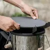 Hands placing a round metal plate on top of a silver cylindrical stove. Produktbild-Vorschau