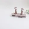 A gray cosmetic headband with two brown snail-like antennae with white eyes is placed on a white background. Produktbild-Vorschau
