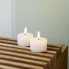Two white LED tea lights with illuminated flames sit on a slatted wooden surface against a pale green and white background. Produktbild-Vorschau