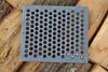 A cast iron grate with many circular holes lies on a surface of stacked wood. Voir les images du produit