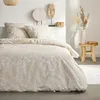 A bedroom scene with a bed dressed in a floral patterned duvet cover and pillows, decorated with various art pieces and a small wooden stool with a vase of dried flowers. Produktbild-Vorschau