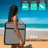 A woman is walking on a beach carrying a folded beach chair over her shoulder. Produktbild-Vorschau
